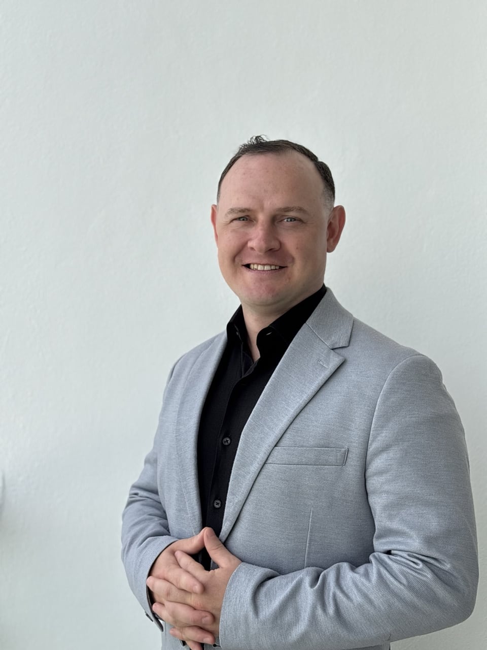 Denis in a gray suit against a light wall